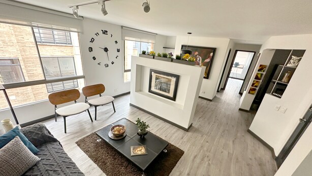 A modern living room with a fireplace, a large clock, and a dining area with chairs.