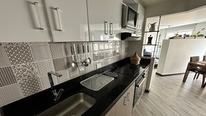 A modern kitchen with a black countertop, stainless steel sink, and patterned backsplash.
