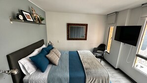 A modern bedroom with a bed, a TV, a chair, and a window.