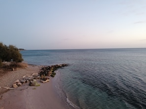 A beach with clear water, a rocky shoreline, and sparse vegetation.