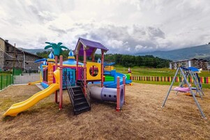 Un parque infantil con tobogán, zona de escalada y columpios.