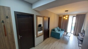 A modern living room with a sofa, a coffee table, and a TV. There is a door with a mirror and a wooden panel on the left. - Bakuriani Crystal Loft 406 (Borjomi)