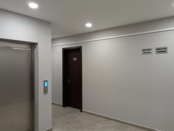 Un pasillo con una puerta identificada como 407, un ascensor y señales indicativas para las habitaciones 401-407 y 408-414.