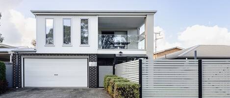 Una casa moderna de dos pisos con garaje, balcón y patio cercado.