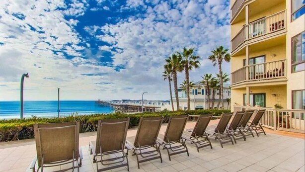 Une terrasse d’hôtel située en bord de mer, avec des chaises longues, une vue sur l’océan et une jetée en arrière-plan.