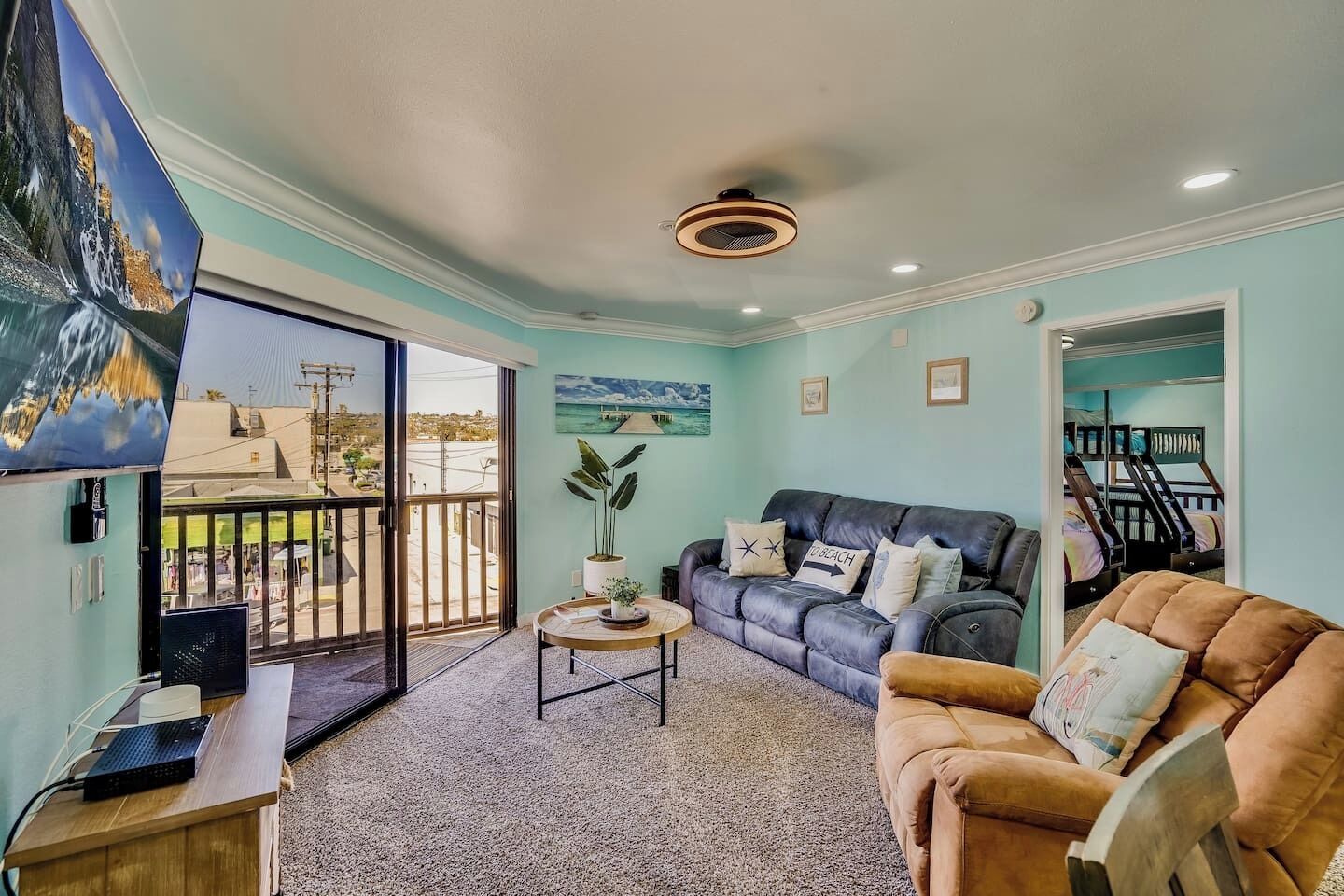 Un salon avec un canapé, une table basse et un téléviseur posé sur un meuble. Il y a un balcon avec vue sur l’extérieur.
