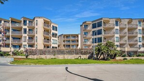 Un immeuble résidentiel à plusieurs étages, doté de balcons, d’une zone pavée devant et surplombant un ciel dégagé.