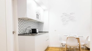 A compact kitchen with a modern design, including a herringbone-patterned backsplash, a built-in microwave, and a small dining area with a round table and white chairs. - Estudio Gaviota by Cadiz Time (Cádiz)