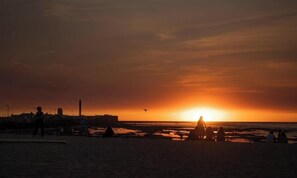 A beach scene with a sunset, silhouettes of people, and a distant cityscape.