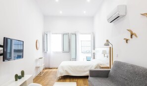 A modern bedroom with a bed, a grey sofa, a desk with a mirror, and a window with curtains.