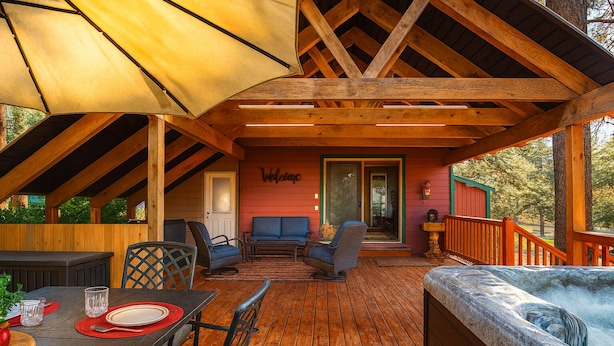 Una terraza exterior con suelo de madera, una zona de estar cubierta con sofá y sillones, una mesa de comedor con sillas y un jacuzzi.