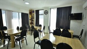 A conference room with multiple tables and chairs, a bookshelf, a clock, and a TV on the wall. - Batumi Hall (Batumi)