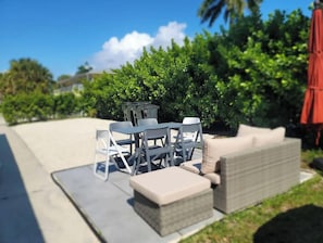 A patio area with a gray outdoor sofa, a small round table, and two chairs. - Singer Island 2 bedroom w/ free parking- no stairs (North unit) (Palm Beach Shores)