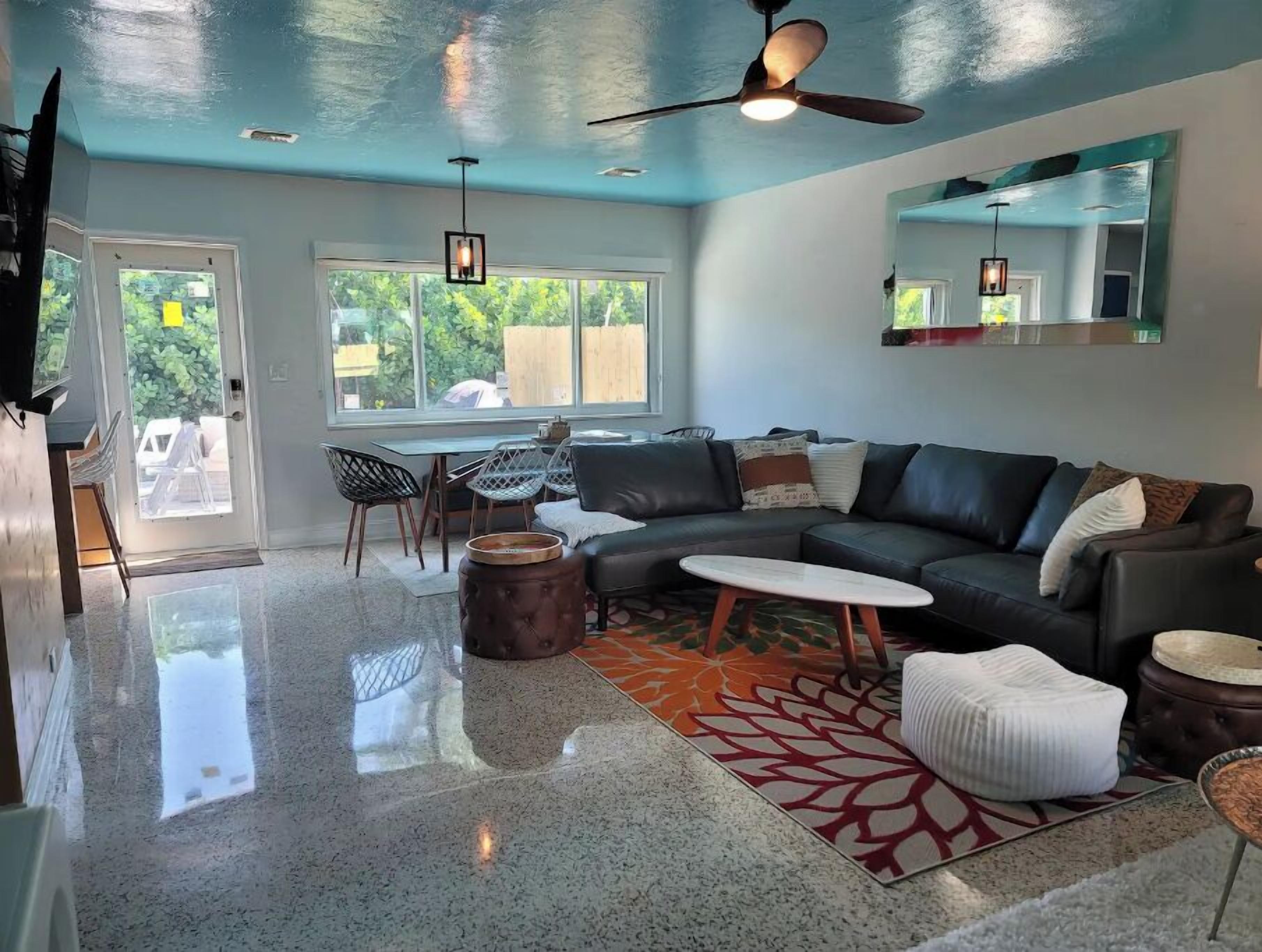 A modern living room with a large window, a ceiling fan, and a dining area with chairs and a table.