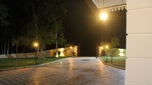A paved pathway leading to a building entrance at night, with street lamps and trees. - Heaven villa (mirissa)