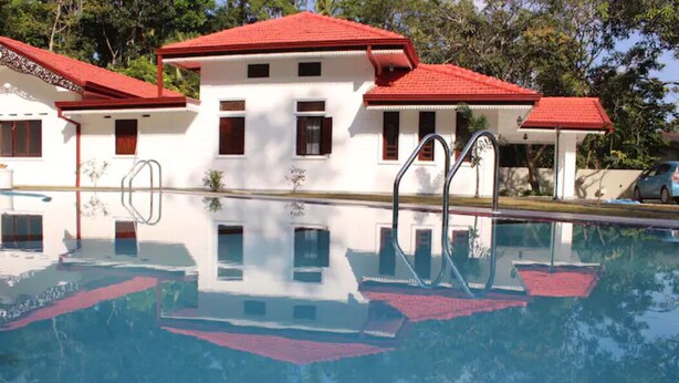 A swimming pool with a reflection of a building with red roofs and white walls. - Heaven villa (mirissa)