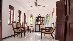 A room with a polished floor, wooden chairs, a ceiling fan, and a door with a traditional design. - Heaven villa (mirissa)