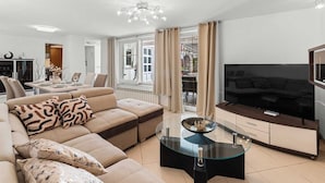 Ett modernt vardagsrum med en soffa, ett soffbord i glas, en tv och en matplats med ett bord och stolar.