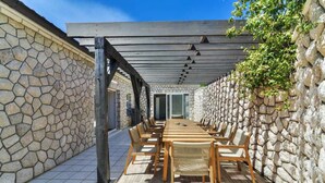 An outdoor patio with a stone wall, wooden pergola, and a long table with chairs. - Villa Luxview 17 Bribir (Bribir)