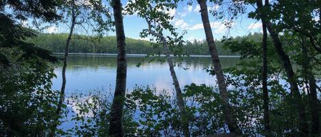 A wooden deck overlooking a calm lake with trees in the foreground.