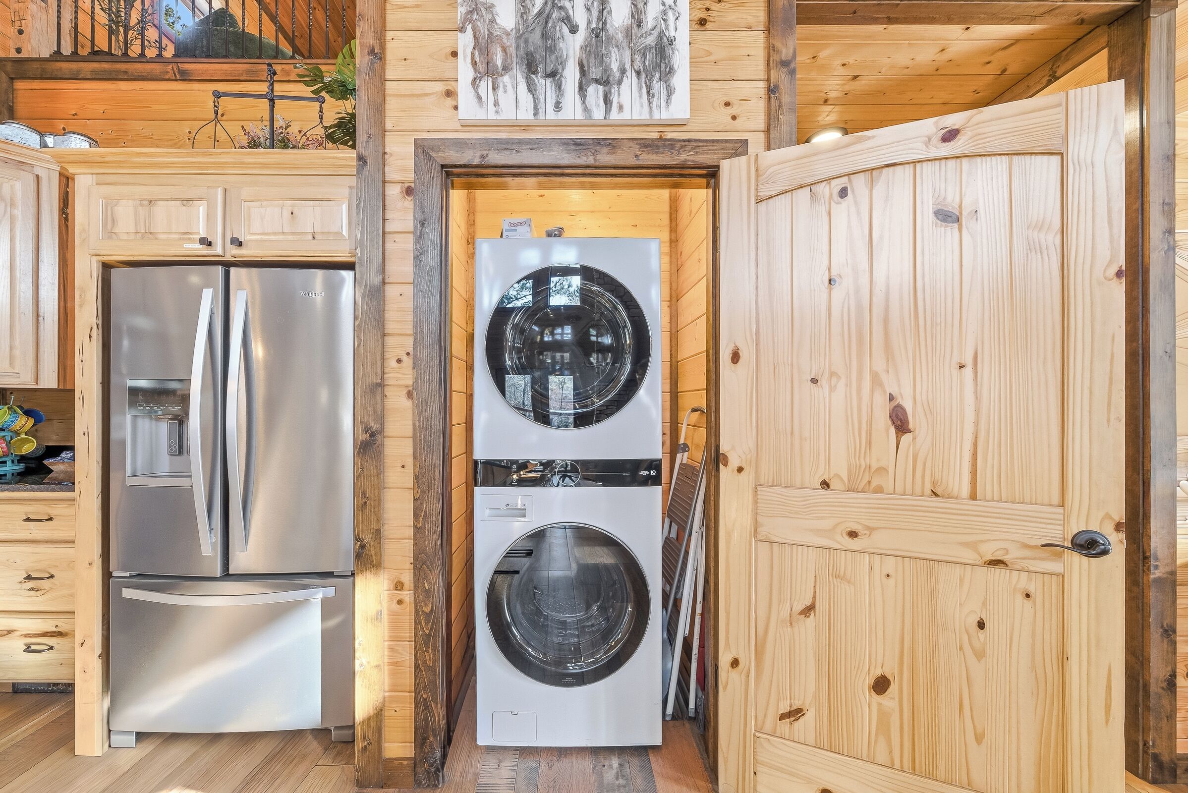 Cocina compacta con refrigerador de acero inoxidable, lavadora y secadora integradas, armarios de madera y techo de madera.
