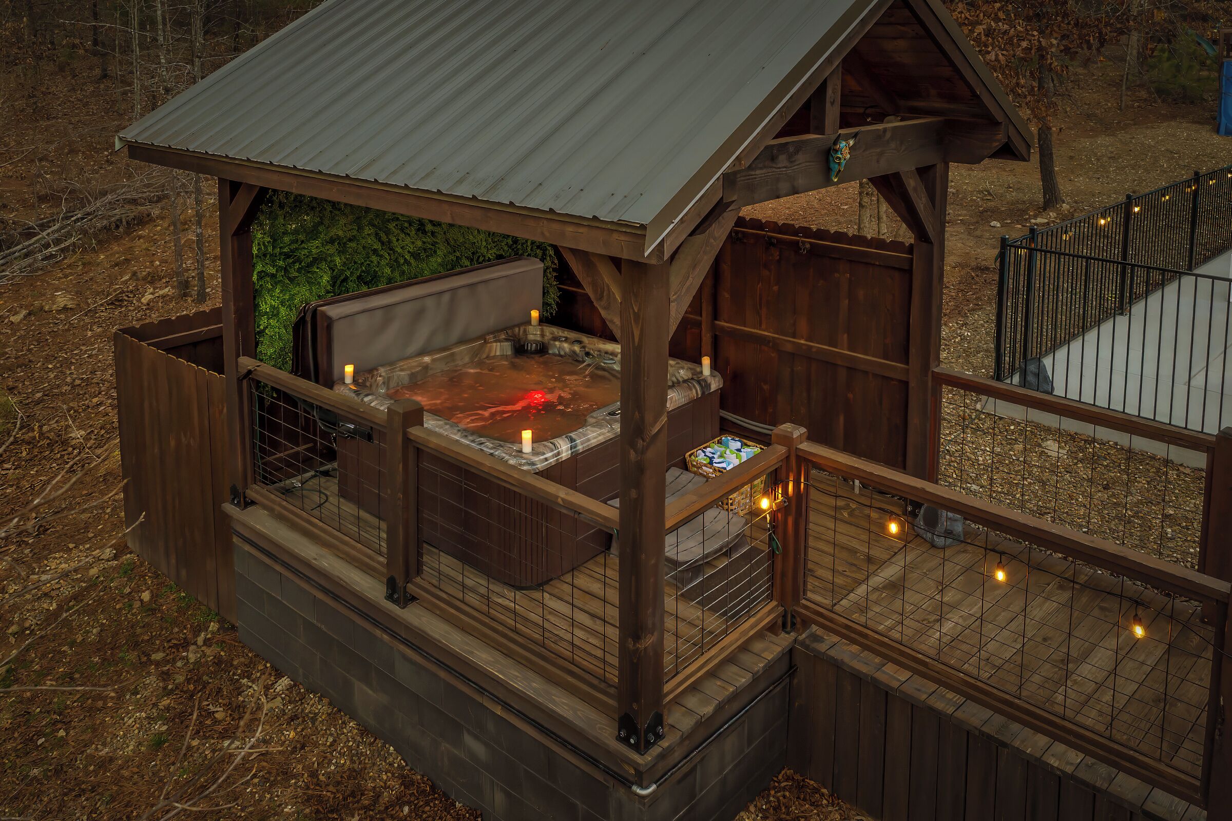 A wooden hot tub structure with a metal roof, surrounded by a wooden deck and railing.