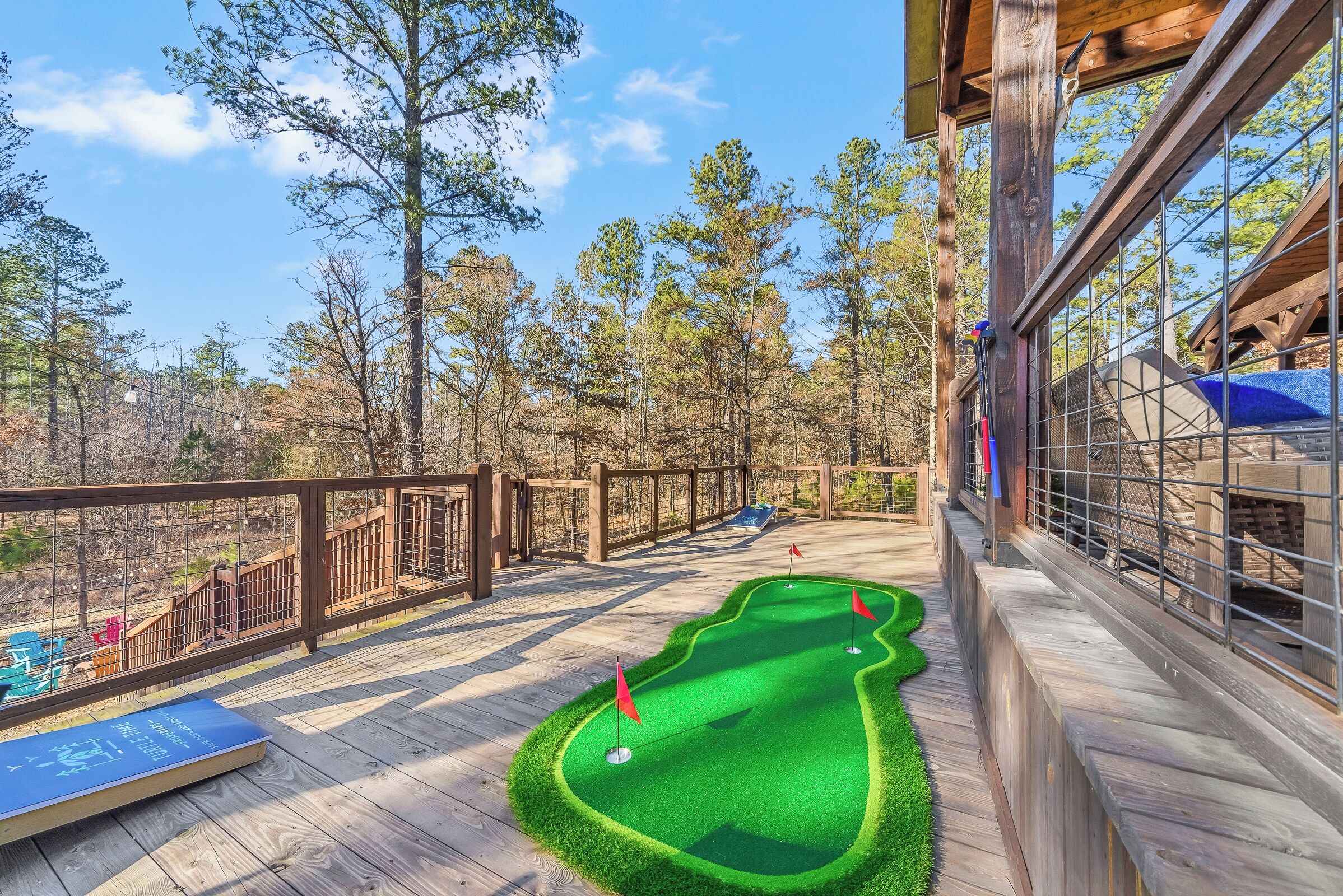 Un campo de mini golf sobre una terraza de madera, con vistas a árboles y un cielo despejado.