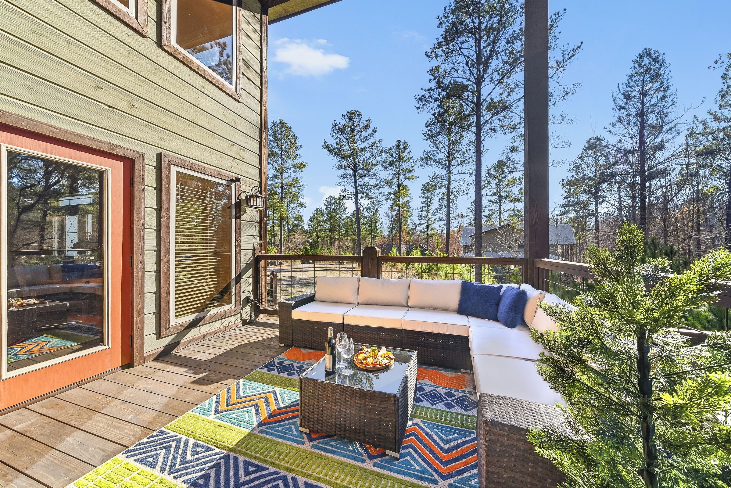 A wooden deck with a sofa and a coffee table, surrounded by a forest.