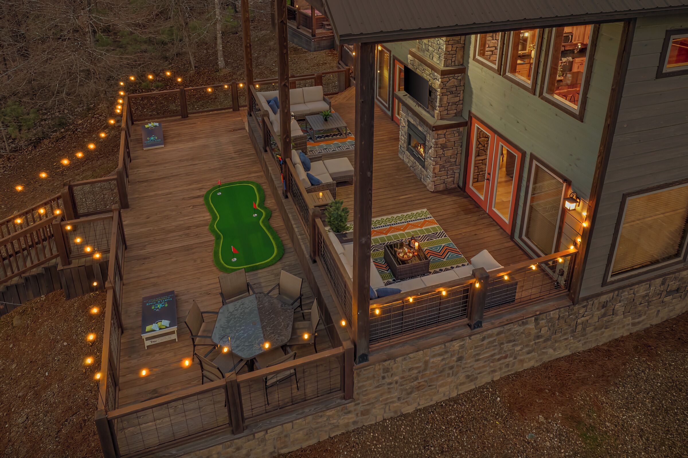 A wooden deck with a putting green, outdoor seating, and a stone fireplace.
