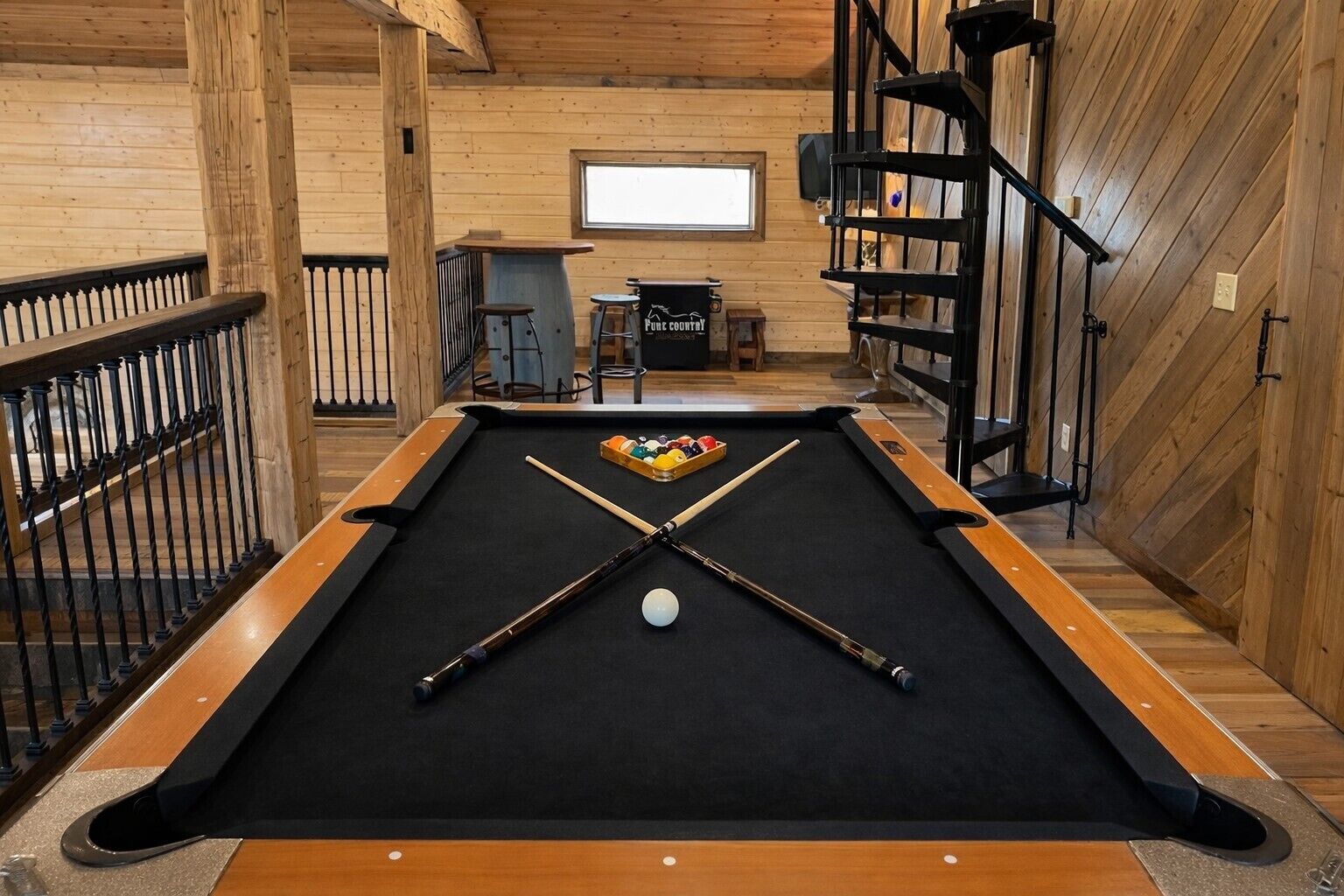 A pool table with a billiard ball and cues, surrounded by wooden walls and a wooden railing.