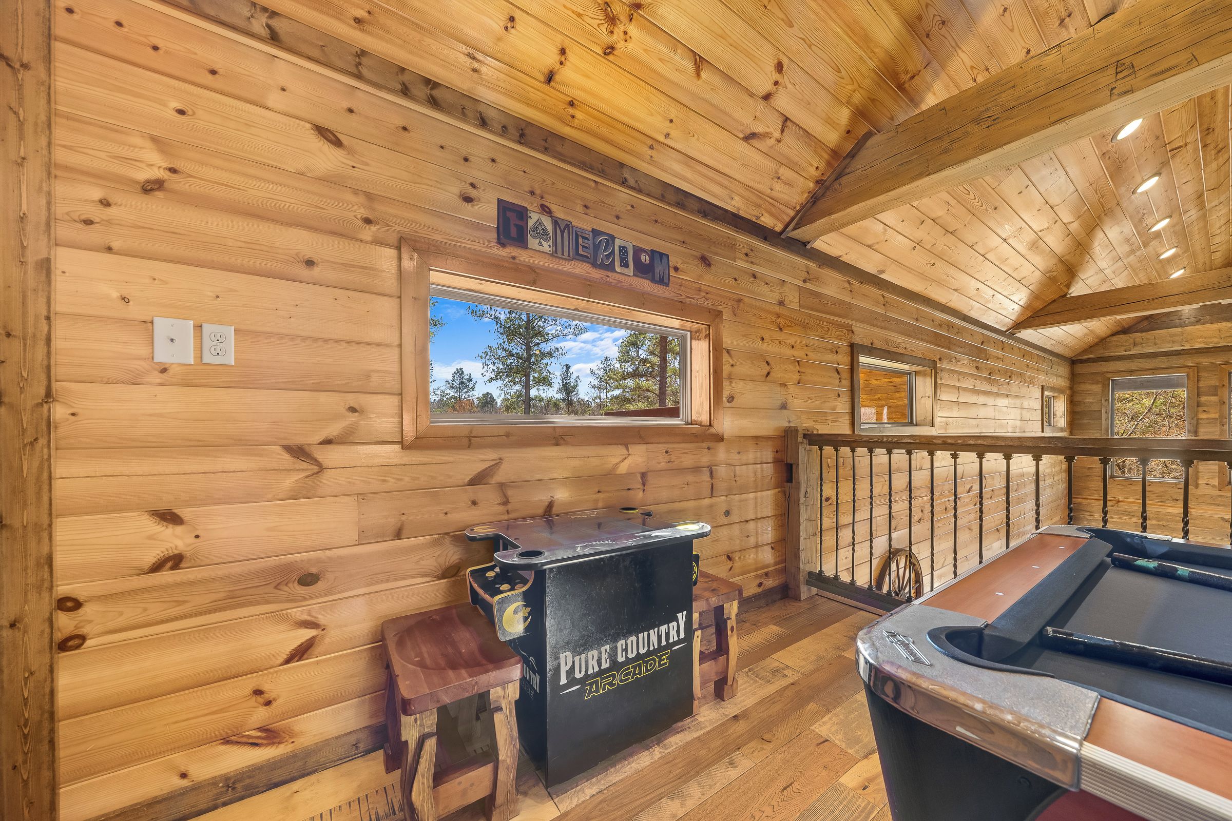 A wooden cabin interior with a pool table, a bar area labeled "PURE COUNTRY ARCADE," and a window overlooking trees.