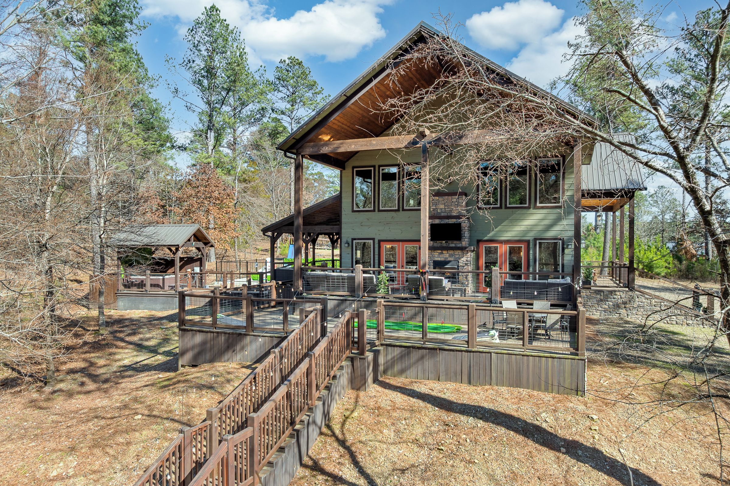 A large, two-story house with a covered patio area, surrounded by trees and a wooden fence.