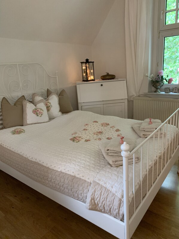 Un lit bien fait, recouvert d’une courtepointe à motifs floraux, une table de chevet avec une lanterne et une fenêtre avec des rideaux.