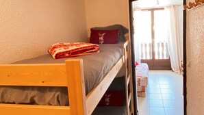 A room with a bunk bed, a small table with a red cushion, and a window with curtains.