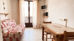 A cozy room with a sofa, a wooden dining table, a TV mounted on the wall, and a window with curtains.