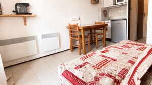 A compact room with a bed, a small table, a chair, a microwave, and a refrigerator.