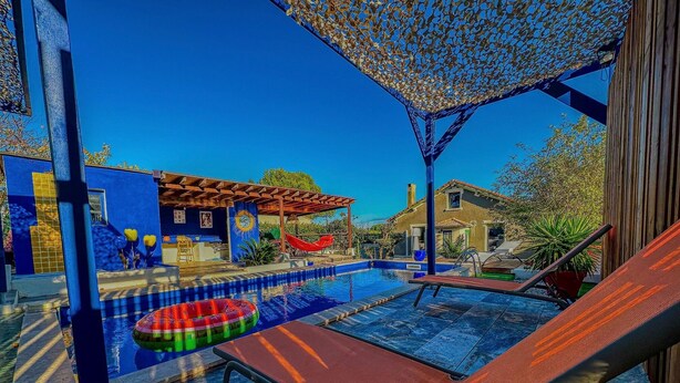 A pool area with lounge chairs, a red hammock, and a blue building with yellow accents. - Le Petit Majorelle Français, Swimming pool Garden Terrace, near city center. (Lavalette)