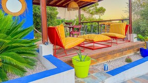 A covered outdoor seating area with red and yellow striped chairs, a wooden deck, and a blue wall with a circular design. - Le Petit Majorelle Français, Swimming pool Garden Terrace, near city center. (Lavalette)