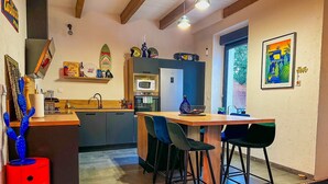 A kitchen with a central island, bar stools, a red barrel, and a tiled floor. - Le Petit Majorelle Français, Swimming pool Garden Terrace, near city center. (Lavalette)