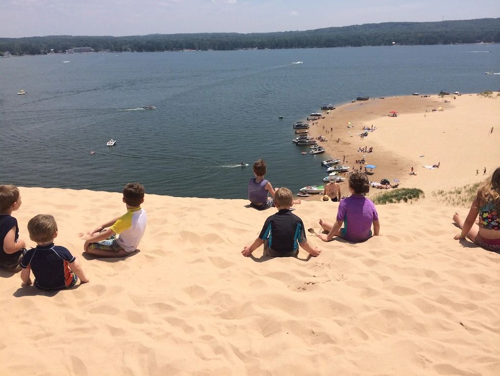 Een strand met kinderen die op het zand zitten, boten in het water en een helder uitzicht op de kustlijn.