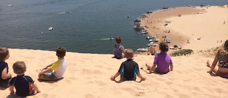 Een strand met kinderen die op het zand zitten, boten in het water en een helder uitzicht op de kustlijn.