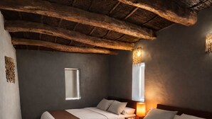 Una habitación con dos camas, techo de madera y una mesita de noche con lámpara.
