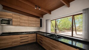 Una cocina moderna con armarios de madera, microondas integrado, estufa a gas y un amplio ventanal con vistas al verdor.