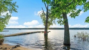 Vista al lago con un muelle que se adentra en el agua, rodeado de árboles y un cielo despejado.