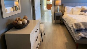 Een slaapkamer met een bed, nachtkastje, lamp en een dressoir met een mand decoratieve items.