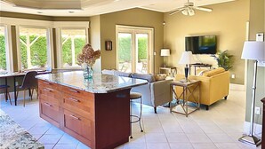 Een ruime woonkamer met een groot keukeneiland, een bank, een televisie en een eethoek met stoelen en een tafel.