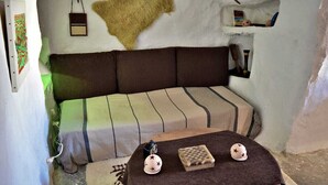 Ein Zimmer mit einer Couch, einem kleinen Tisch mit Schachbrett und Hut, sowie einer Wand mit Fellteppich und Werkzeugen.