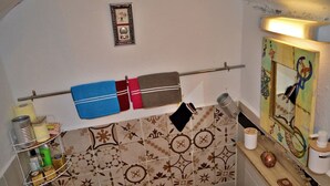 Ein Badezimmer mit gemusterten Fliesen, einem Handtuchhalter mit mehreren Handtüchern, einer Ablage für Toilettenartikel und einem dekorativen Spiegel.