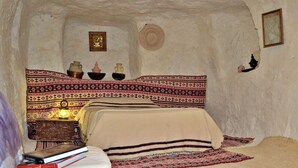Ein gemütliches Zimmer mit einem Bett, einem kleinen Tisch mit Lampe und einem an der Wand befestigten Regal mit Dekoration.
