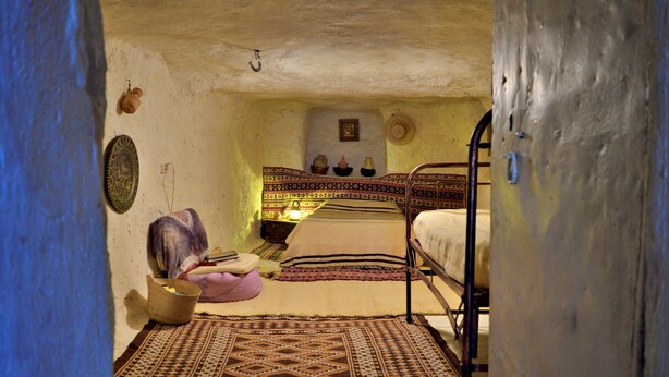 Ein traditionell eingerichteter Raum mit einem Bett, einem kleinen Tisch und einer Wandregal mit Dekoration.